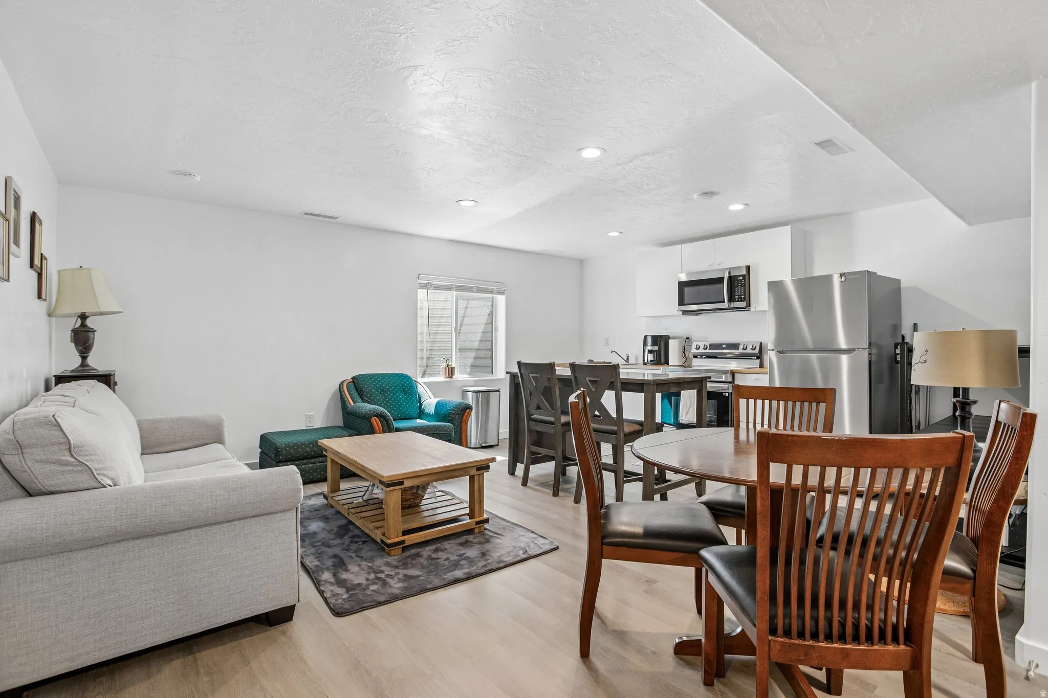 Open-concept living space featuring wood-finish flooring, recessed lighting, and a white kitchen with stainless steel appliances