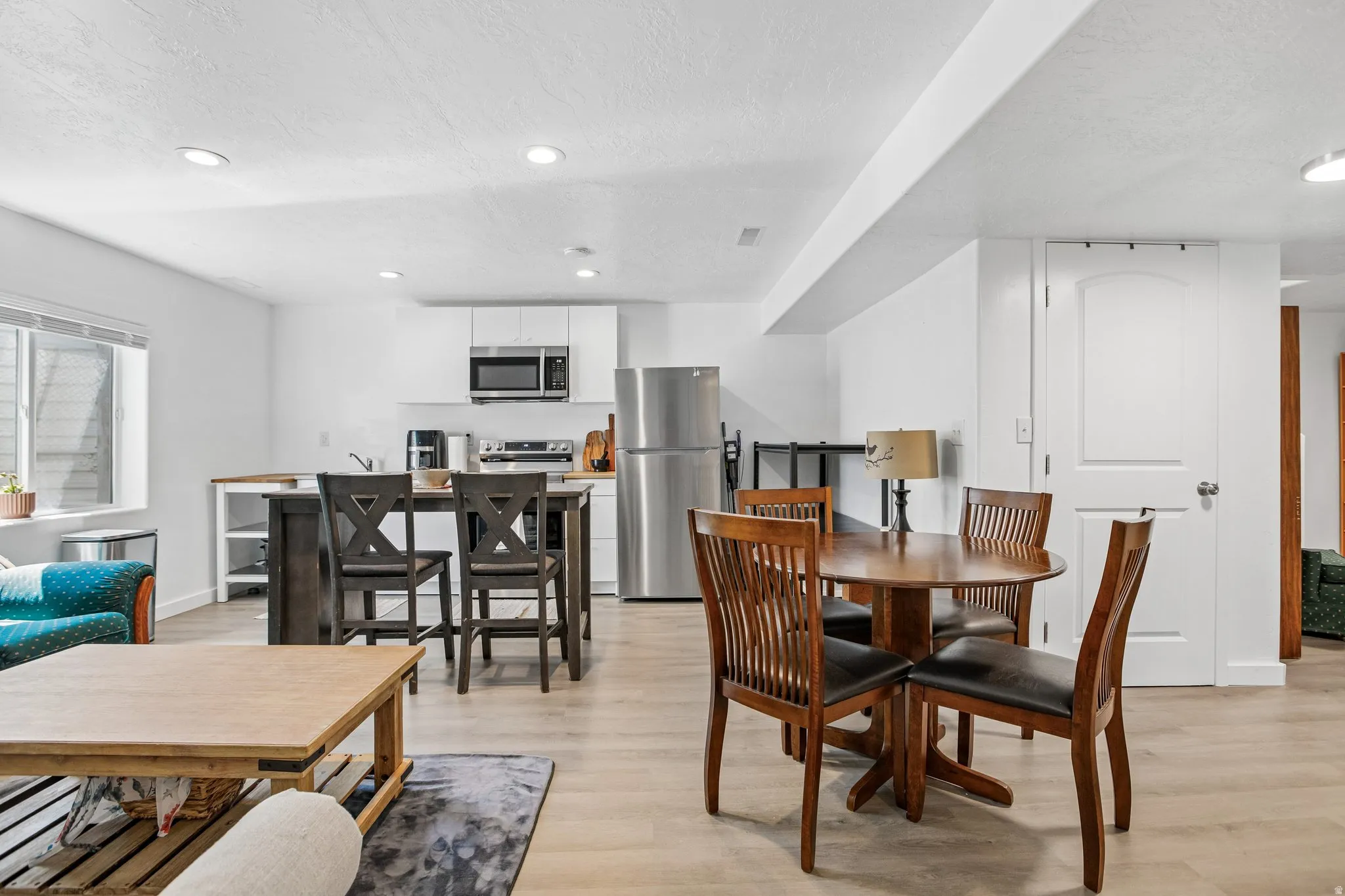 Open-concept living area with wood-finish flooring, recessed lighting, and a modern kitchen featuring white cabinetry, stainless steel appliances, and a wood countertop island