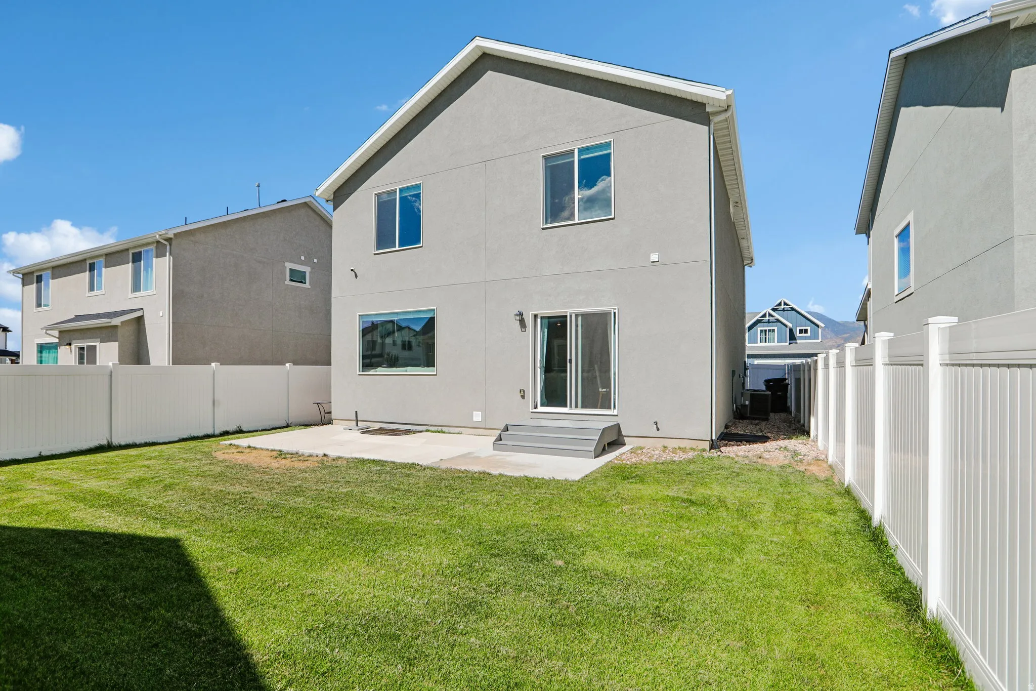 Expansive grass lawn with a concrete patio, white vinyl fencing, and sliding glass door access