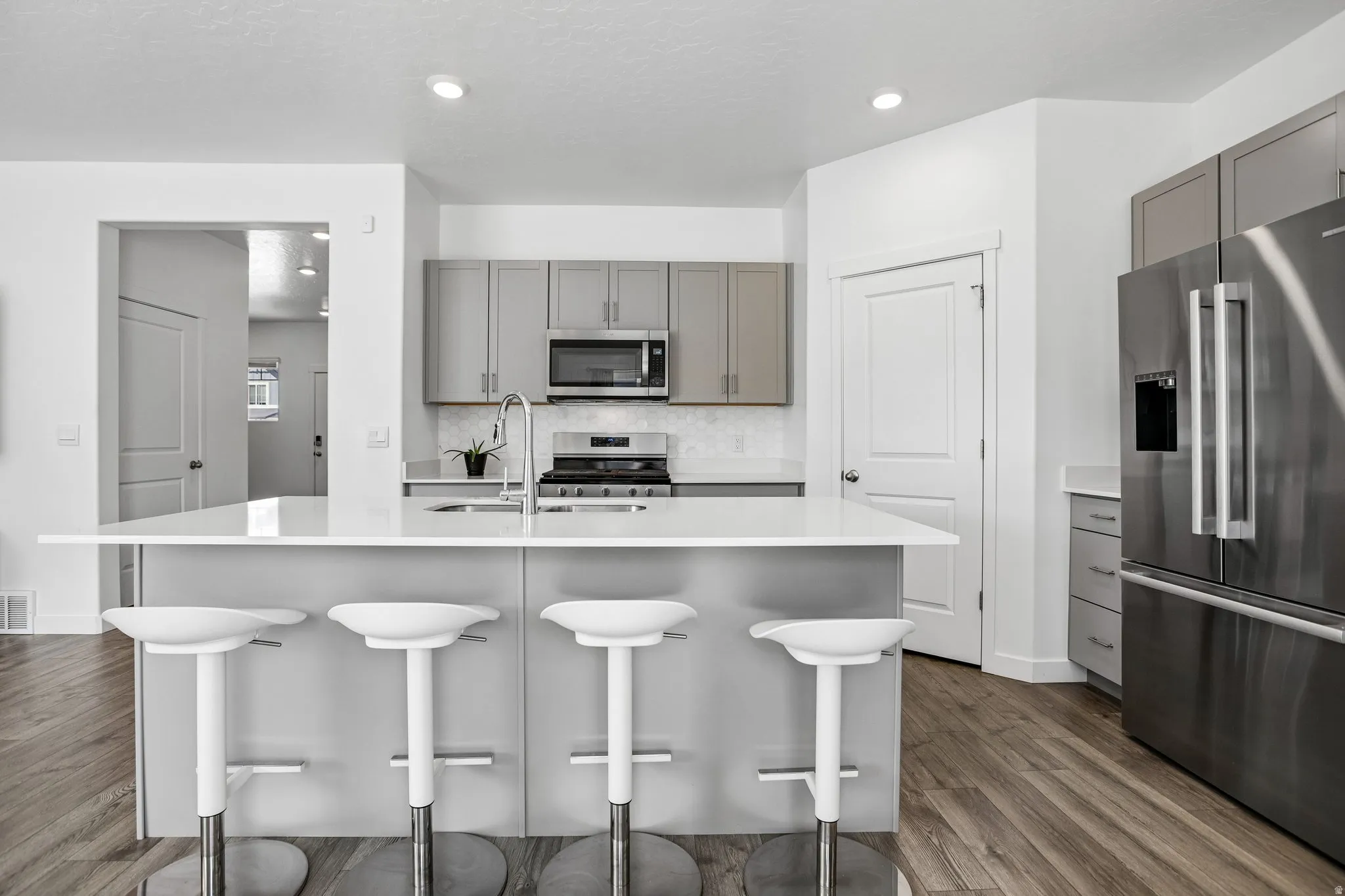 Kitchen island with a white countertop and seating, stainless steel appliances, grey cabinetry, and wood-finish flooring