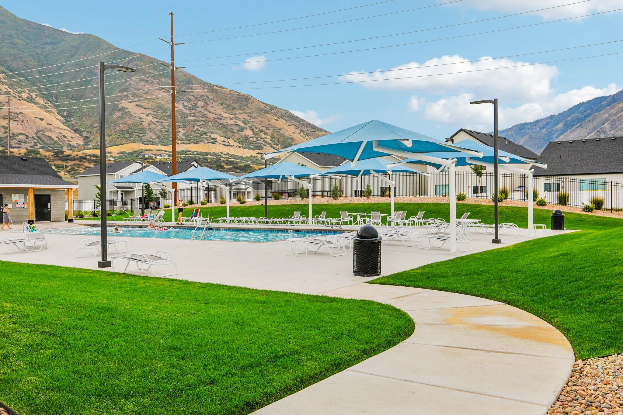 Community swimming pool with a surrounding concrete deck, multiple shade structures, and a manicured lawn