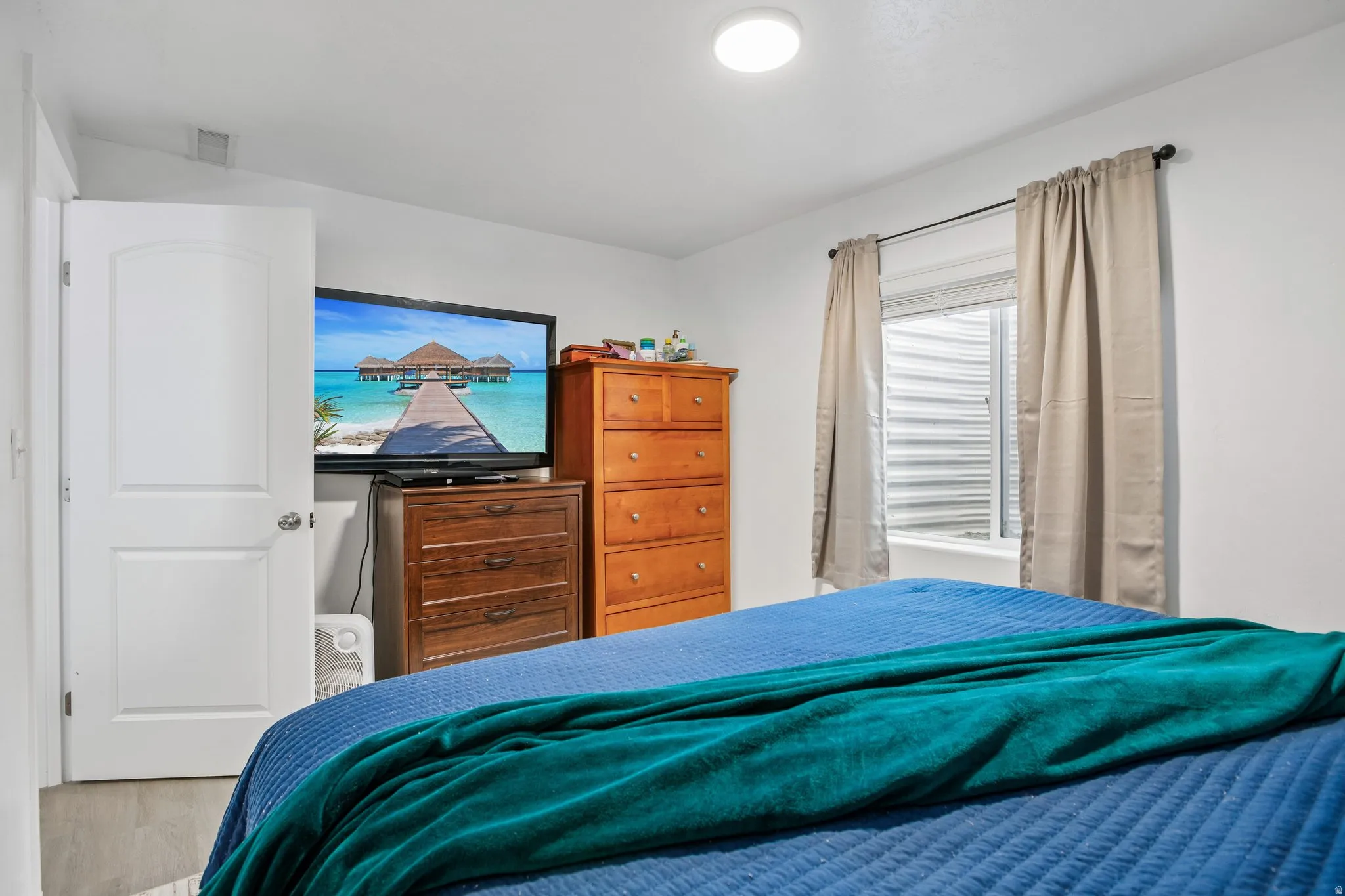 White interior walls with a window featuring blinds, a white door with a paneled design, and wood-finish flooring