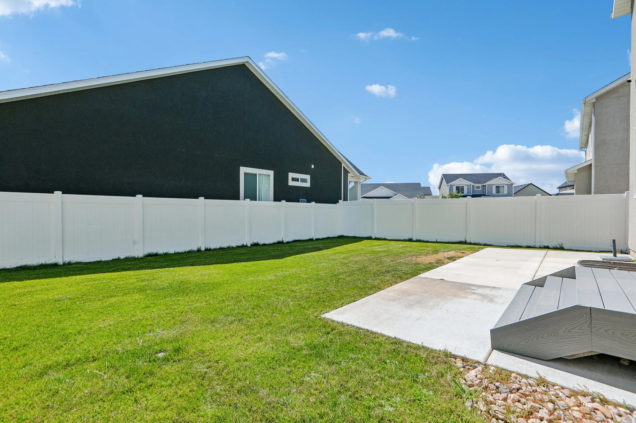 Expansive lawn area with a white privacy fence, concrete patio, and composite decking