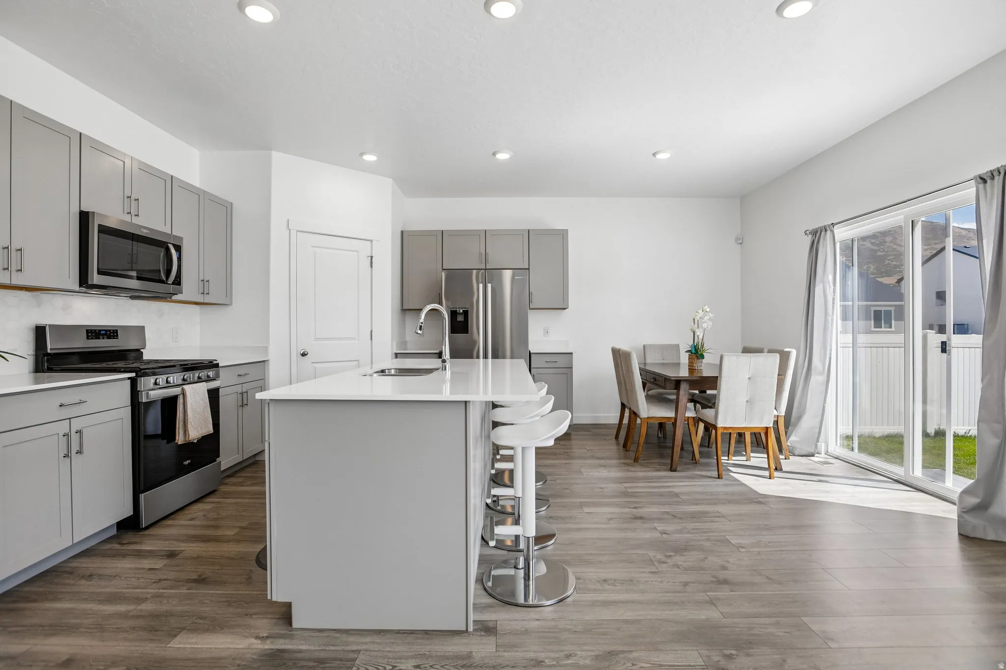 Open-concept kitchen featuring gray cabinetry, stainless steel appliances, a white island with seating, and wood-finish flooring