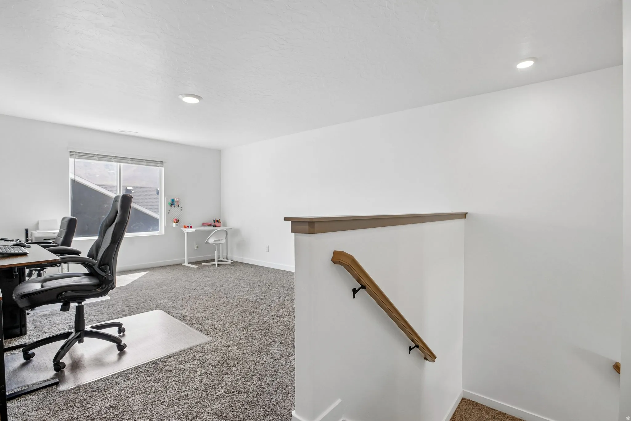 Spacious carpeted area featuring a large window, recessed lighting, and a wood-finish handrail