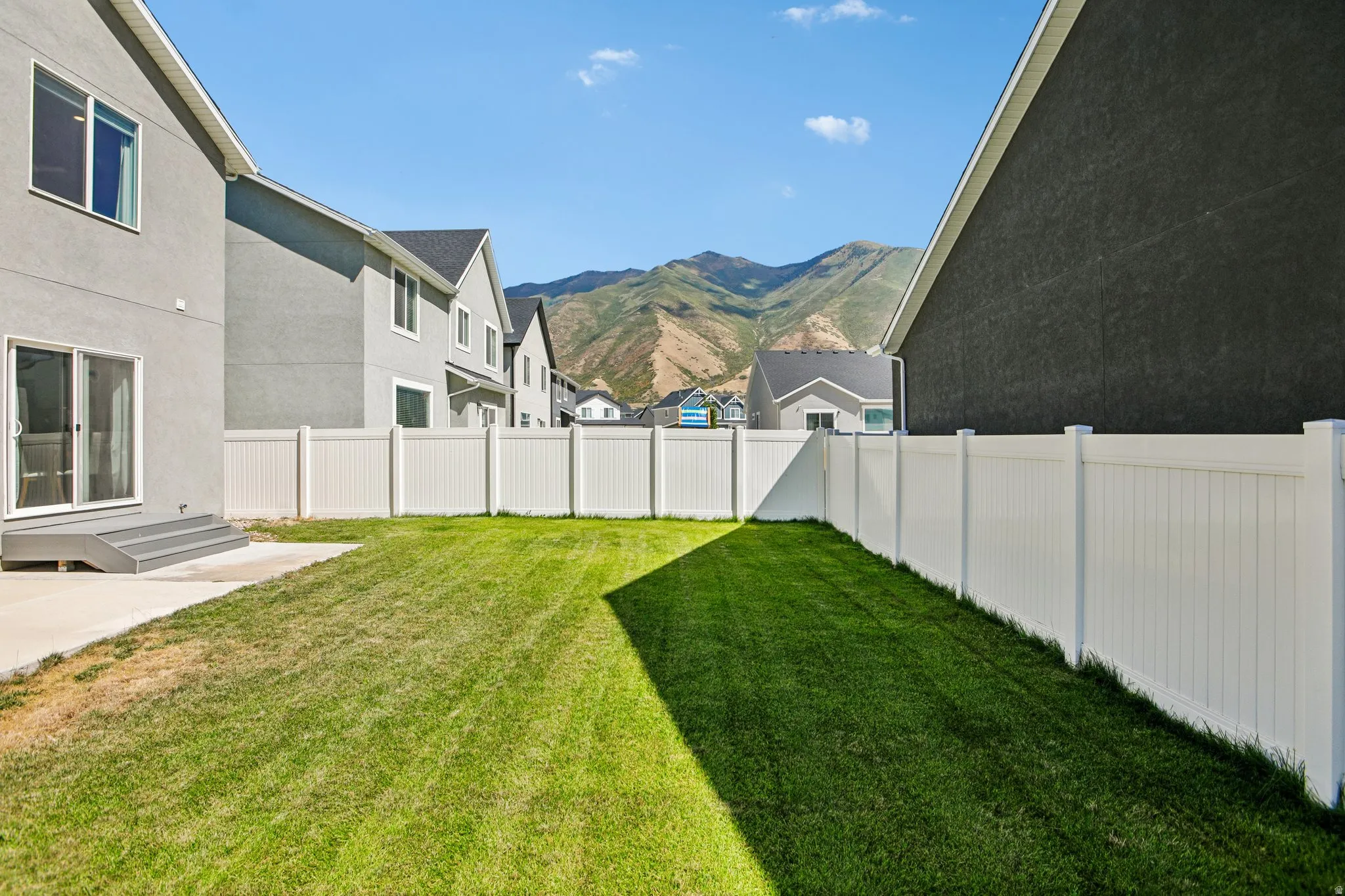 Expansive backyard featuring a manicured lawn, full privacy fencing, and a concrete patio