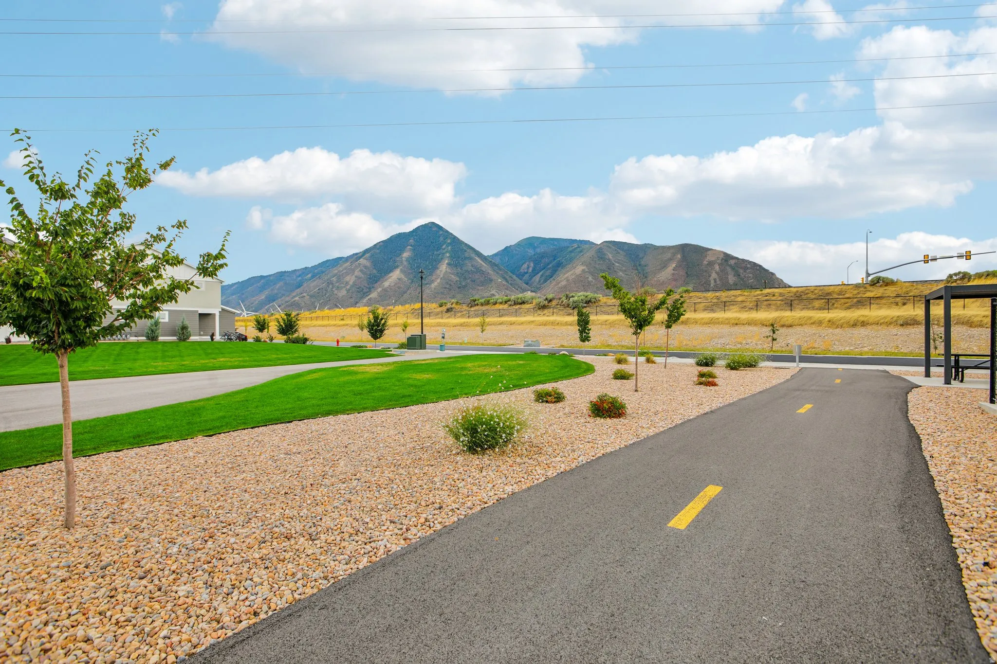 Paved pathway with yellow center line, bordered by gravel landscaping, mature trees, and manicured lawn