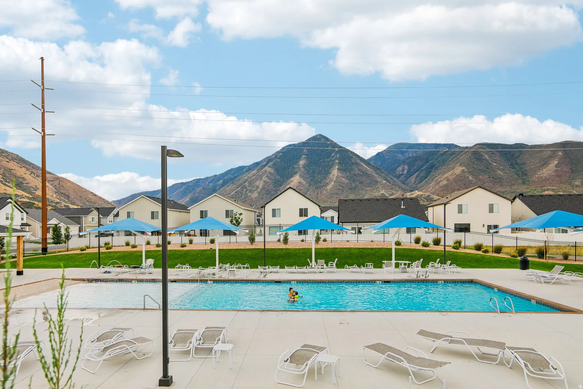 Community swimming pool with an integrated shallow wading area, surrounded by a concrete deck and a manicured lawn