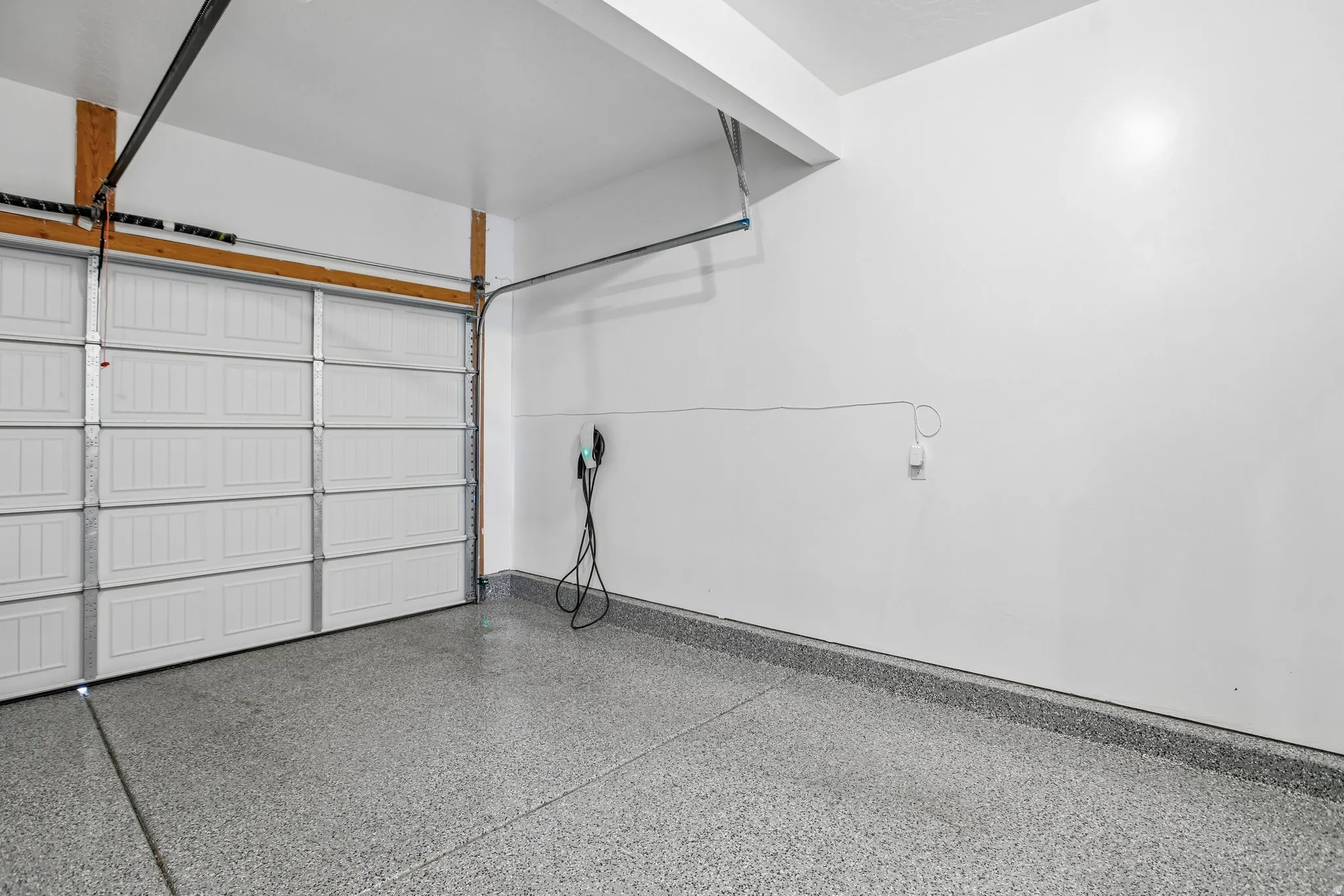 Garage with a white sectional door, grey speckled flooring, and an electric vehicle charging station