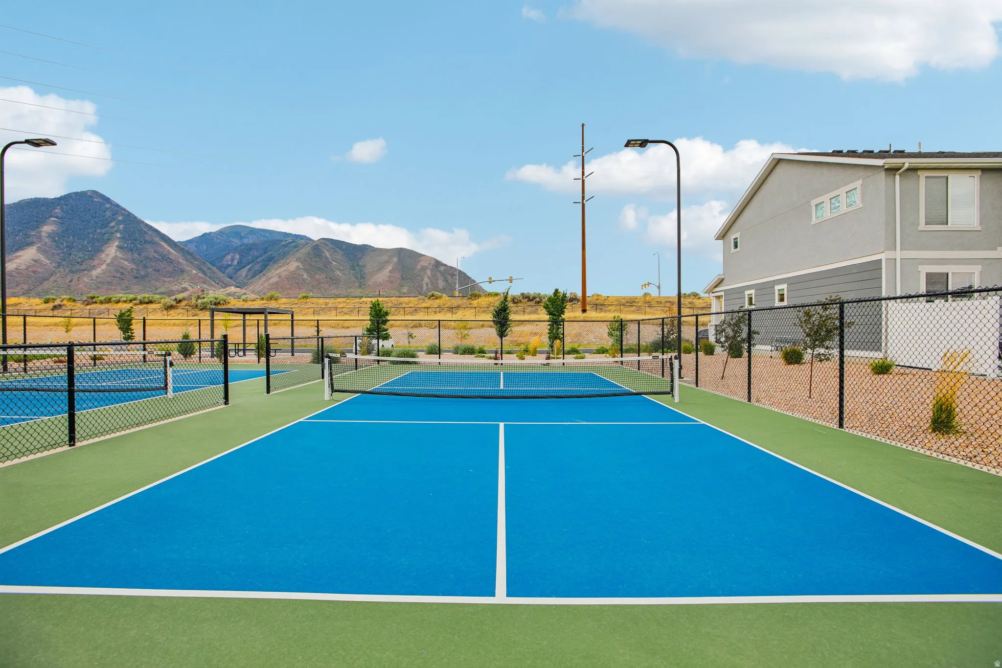 Multiple outdoor courts featuring blue and green surfacing, black chain-link fencing, and overhead lighting