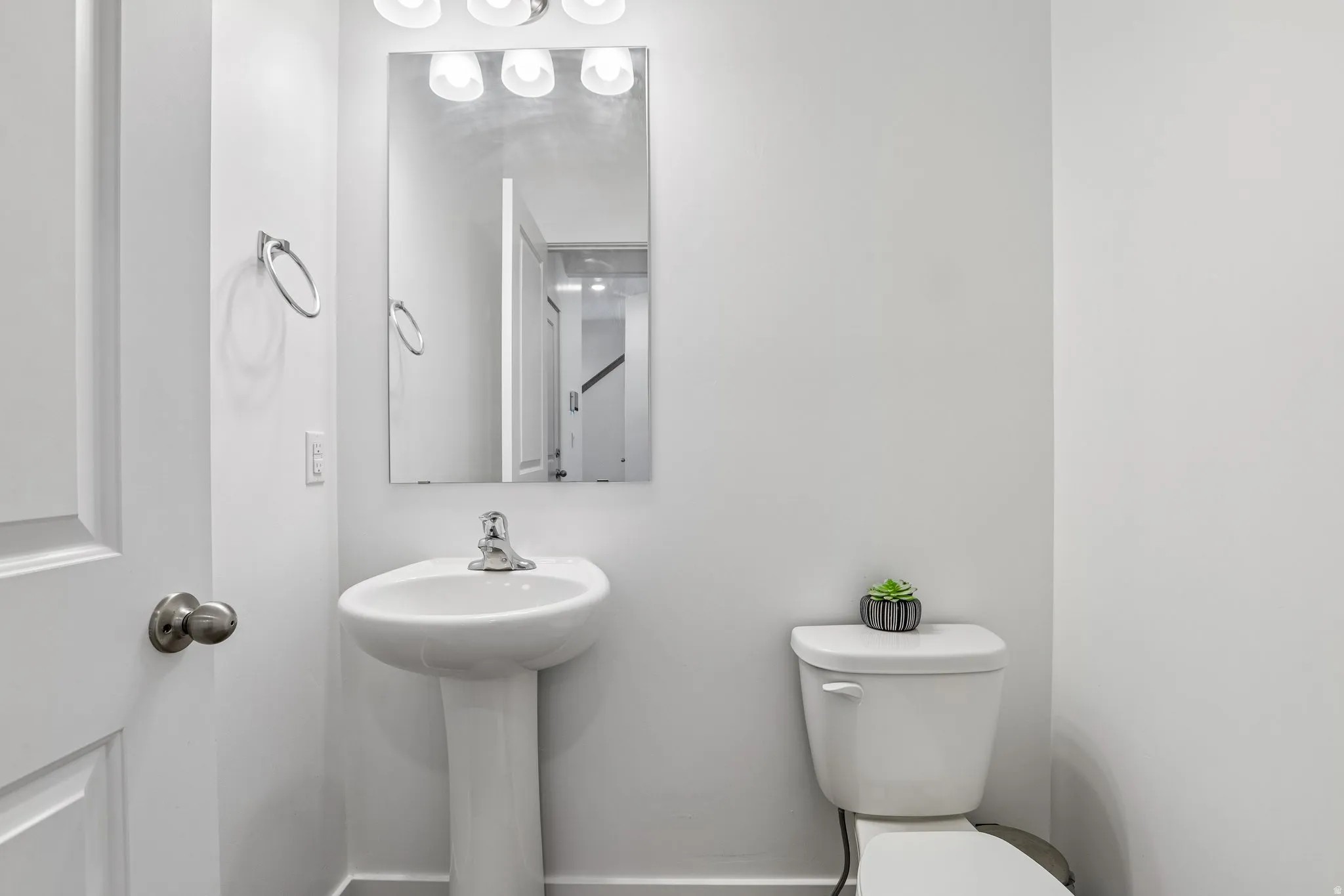 Pedestal sink with chrome faucet, wall-mounted rectangular mirror, and four-light vanity fixture