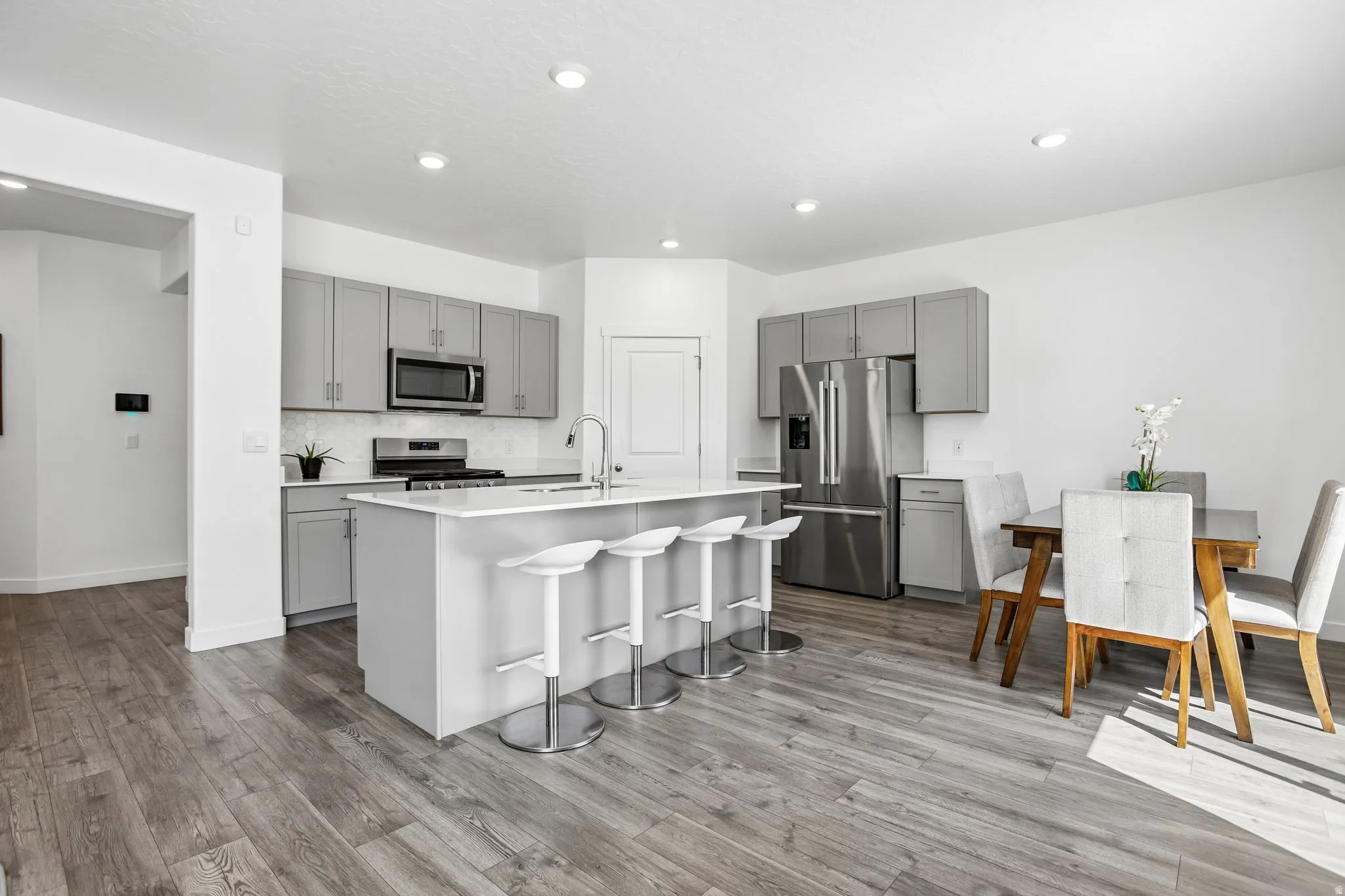 Kitchen featuring wood-finish flooring, recessed lighting, light gray cabinetry, stainless steel appliances, and a central island with an integrated sink