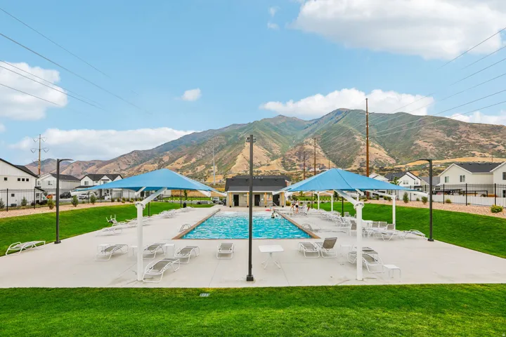 Outdoor swimming pool with a concrete deck, two blue shade structures, and a surrounding grass area