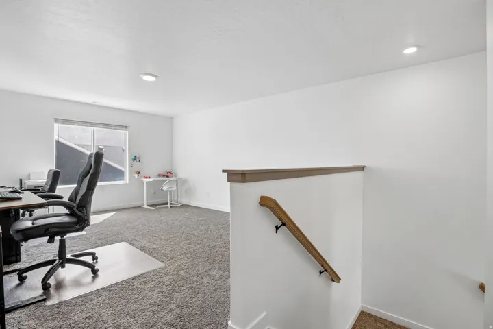 Spacious carpeted area featuring a large window, recessed lighting, and a wood-finish handrail