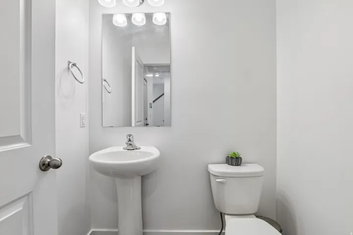 Pedestal sink with chrome faucet, wall-mounted rectangular mirror, and four-light vanity fixture