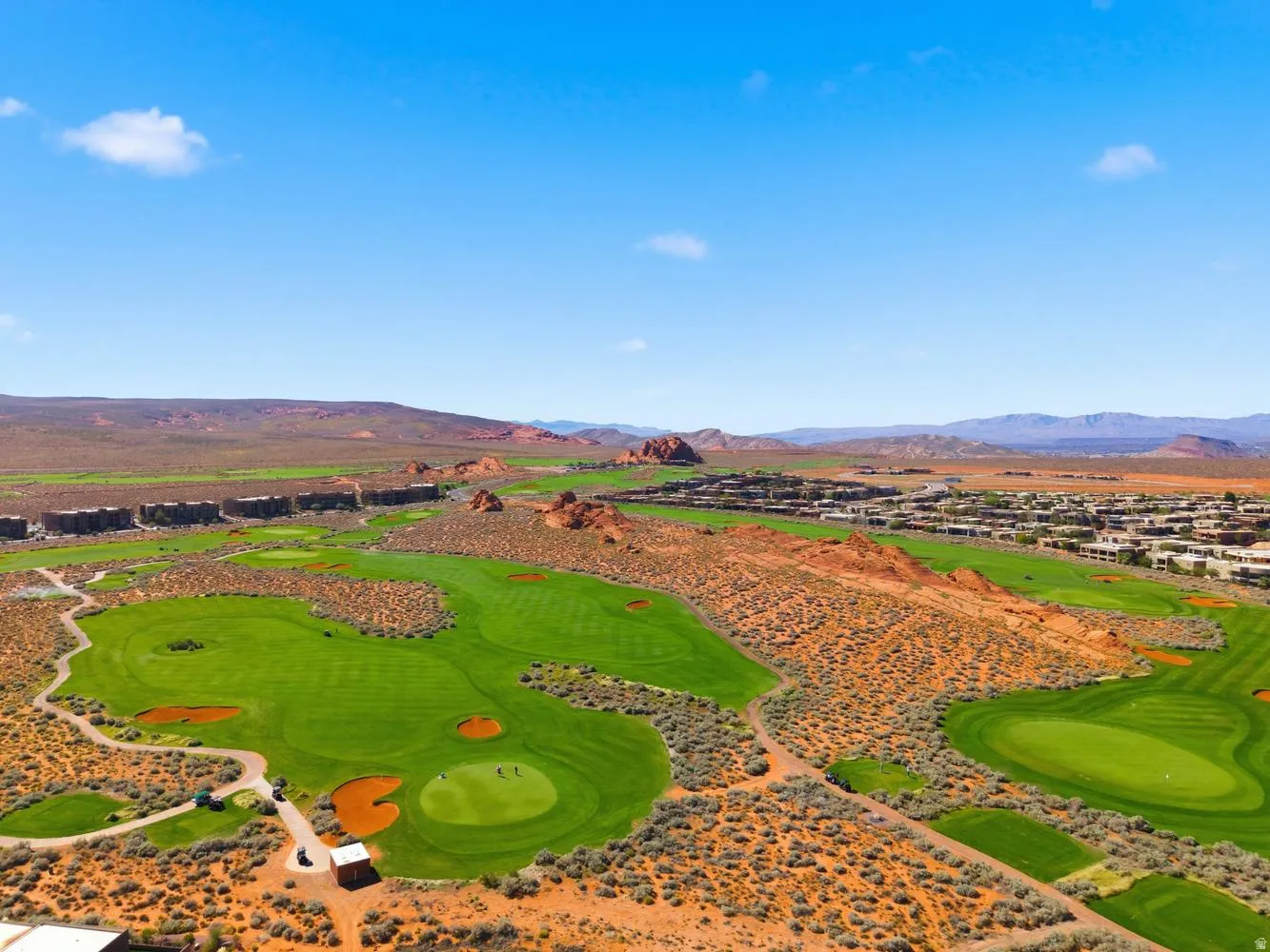 Expansive golf course setting featuring green fairways, red rock formations, and surrounding residential structures