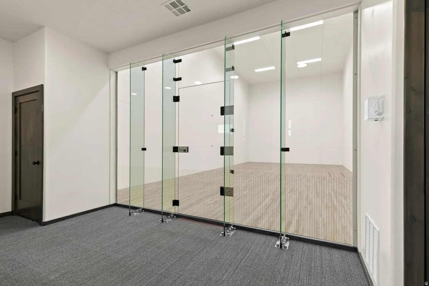 Dedicated racquetball court with a wood-finish floor and full glass enclosure