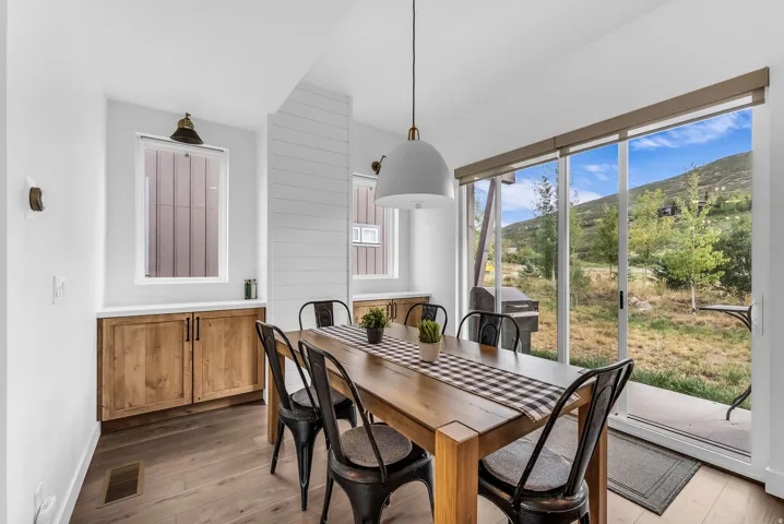 Wood-finish flooring, sliding glass patio doors, shiplap accent wall, built-in cabinetry with a light-toned countertop, and modern pendant lighting