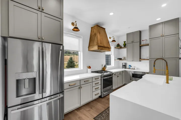 Well-appointed kitchen featuring a wood-finish range hood, stainless steel appliances, light gray cabinetry, crisp white countertops, and wood-finish flooring