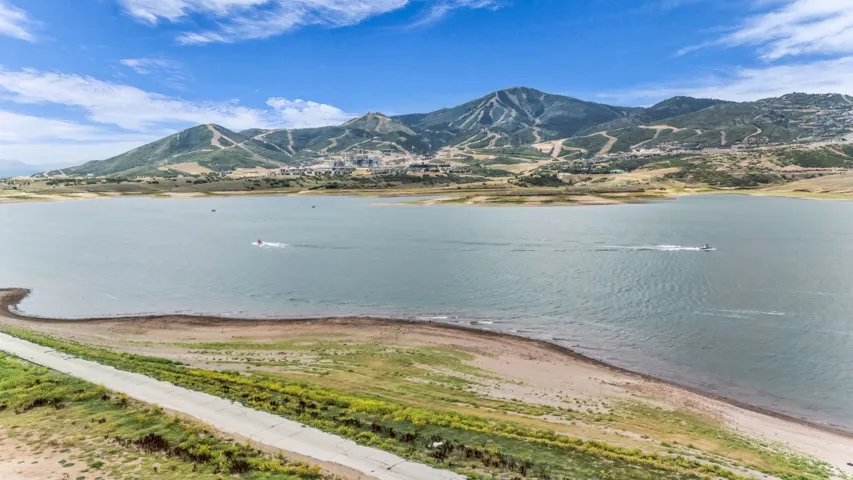 Expansive lake with a concrete path along the shore, surrounded by natural terrain and distant mountains