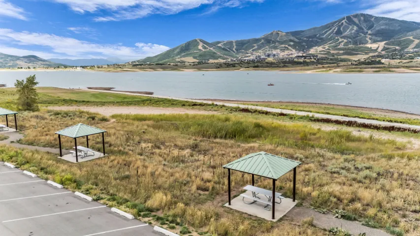 Waterfront setting featuring a mountain backdrop, paved parking area, and covered picnic structures