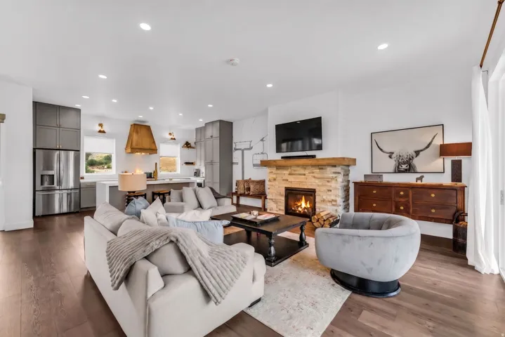 Wood-finish flooring throughout, featuring a stone-clad fireplace with a wood mantle, recessed lighting, and a modern kitchen with stainless steel appliances and full-height cabinetry