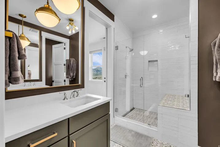 Spacious bathroom featuring a frameless glass shower enclosure with a built-in bench, a single vanity with a white countertop and dark cabinetry, and brass-tone pendant lighting