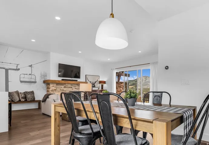 Open-concept living space featuring wood-finish flooring, a stone-clad fireplace with a wood mantle, and sliding glass doors revealing a mountain landscape