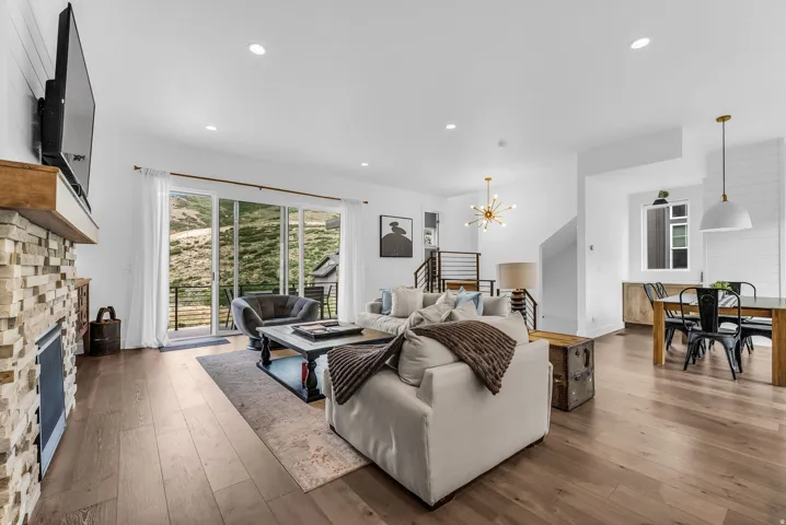 Open-concept living area with wide plank wood-finish flooring, recessed lighting, and a stone-clad fireplace with a wood mantel