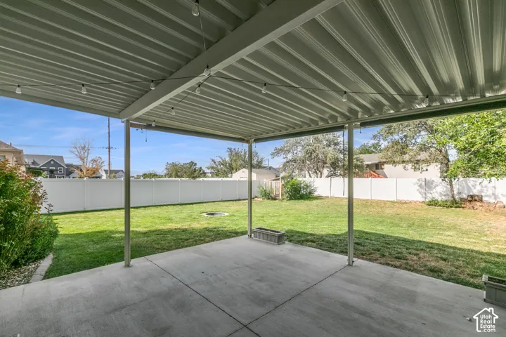 Covered patio with string lighting, concrete flooring, and a fully fenced backyard featuring a grassy lawn