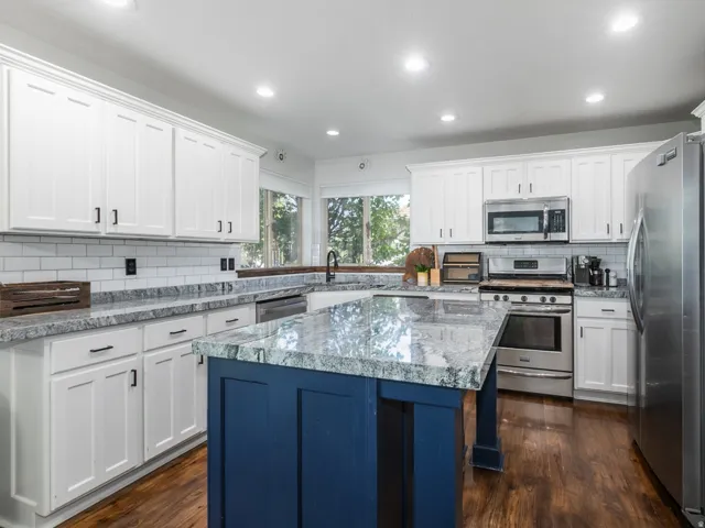 Kitchen featuring white shaker-style cabinetry, granite countertops, subway tile backsplash, stainless steel appliances, and a central island with a navy base