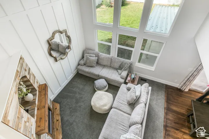 Vaulted ceiling with board and batten wall treatment, large fixed-pane windows, wood-finish flooring, and a built-in fireplace with a wood mantel