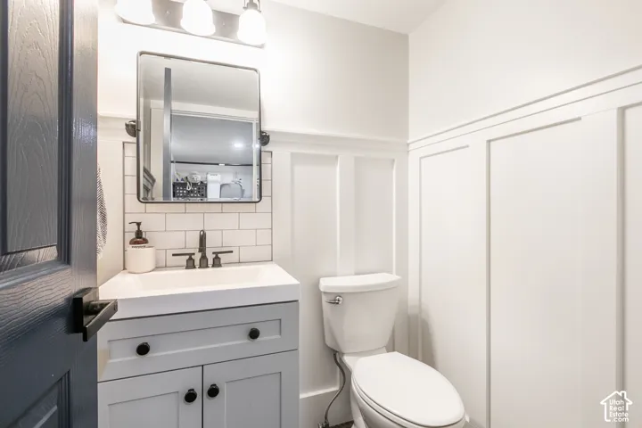 White paneling with trim, gray vanity with black hardware, subway tile backsplash, and a wall-mounted mirror in this 1/2 bath located off the dining room.