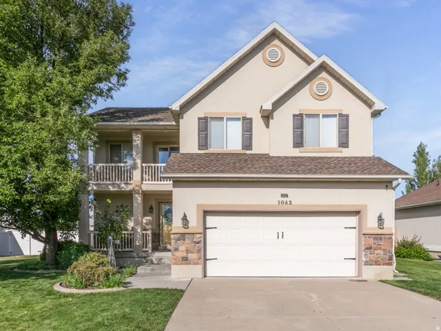Stucco exterior featuring decorative stone accents, a two-story design, an attached garage, and a second-story balcony