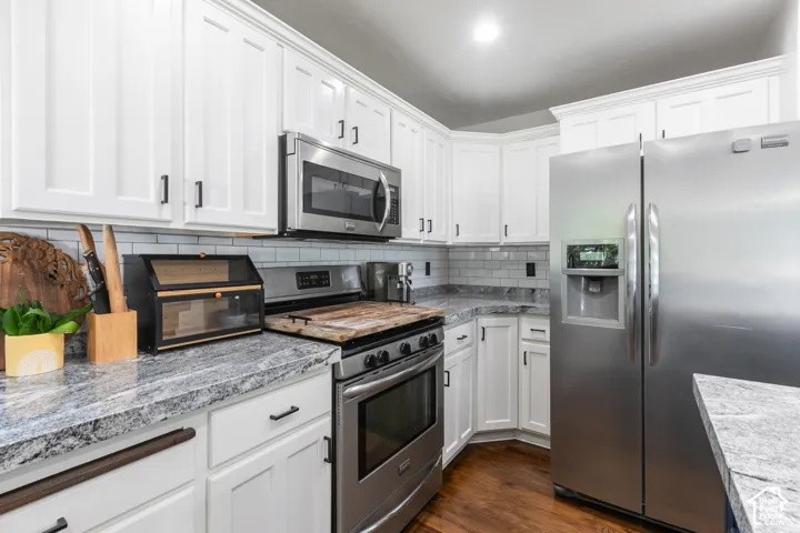 White shaker-style cabinetry, stainless steel appliances, light-toned patterned countertops, subway tile backsplash, and wood-finish flooring