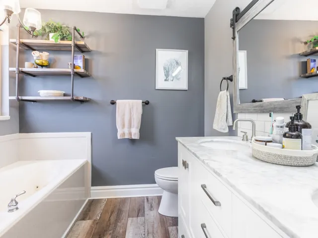 Primary en-suite with Dual vanity, white cabinetry, marble-finish countertop, and laminate hardwood flooring.