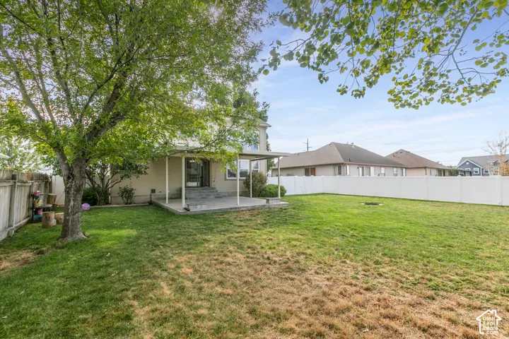 Expansive grass yard with a mature tree, concrete patio, and white privacy fencing