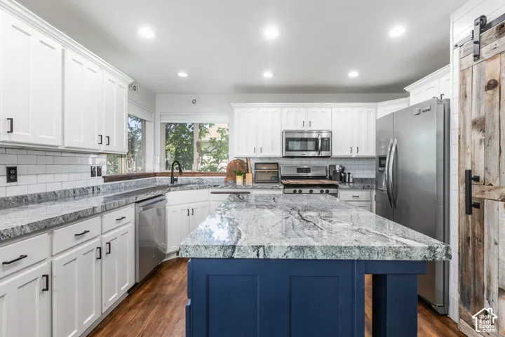 Kitchen featuring white shaker-style cabinetry, a contrasting blue island with a stone countertop, stainless steel appliances, wood-finish flooring, and a white subway tile backsplash