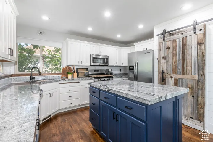 Kitchen featuring white cabinetry, a central island with a blue base, granite countertops, wood-finish flooring, and a barn door leading to large pantry area.