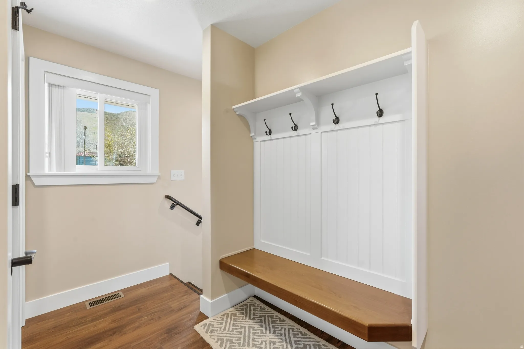 Built-in mudroom bench with wood-finish top and beadboard backing, accented by black metal hooks
