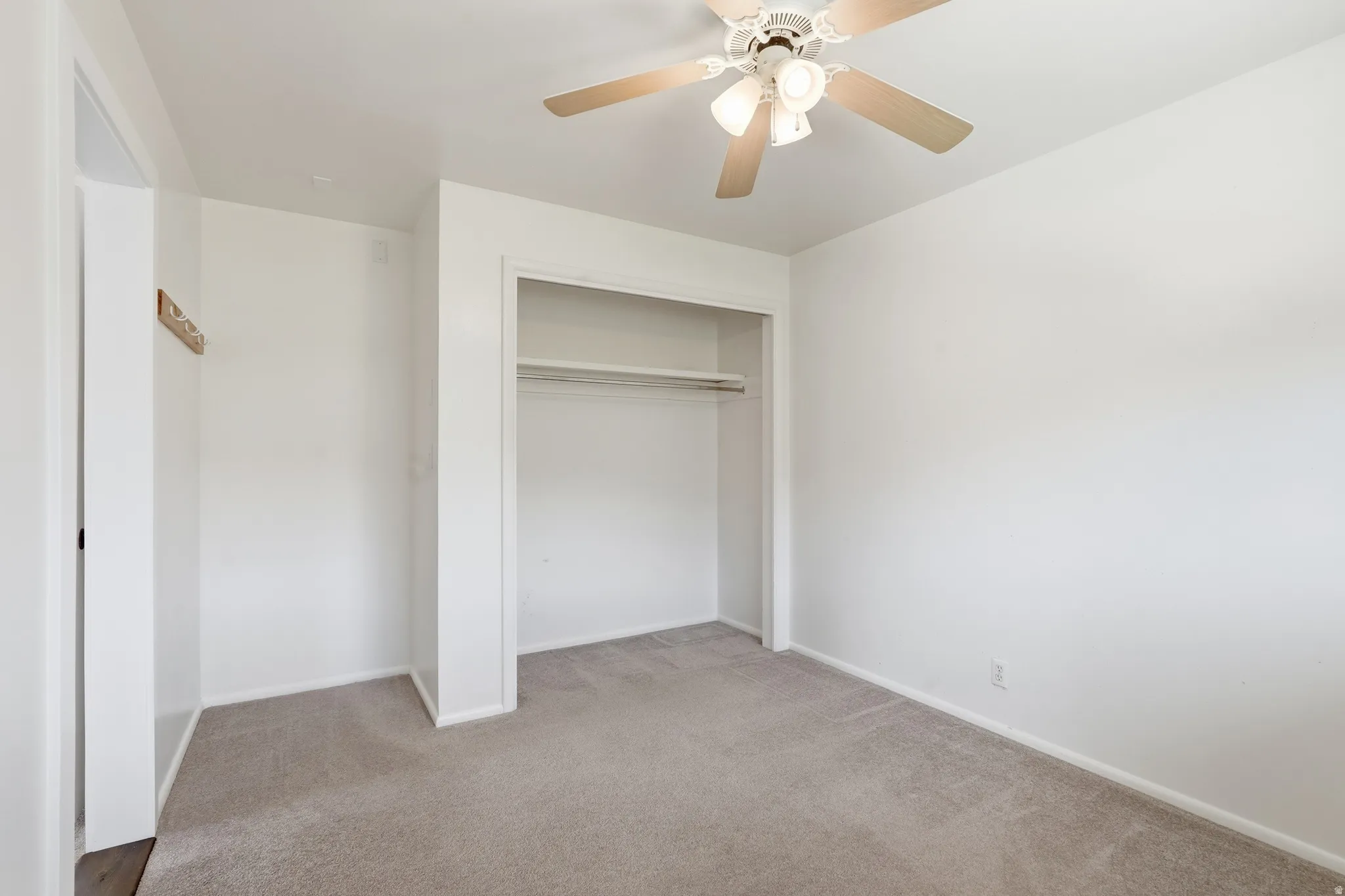 Carpeted room featuring a ceiling fan, closet with shelving and hanging rod, and white walls