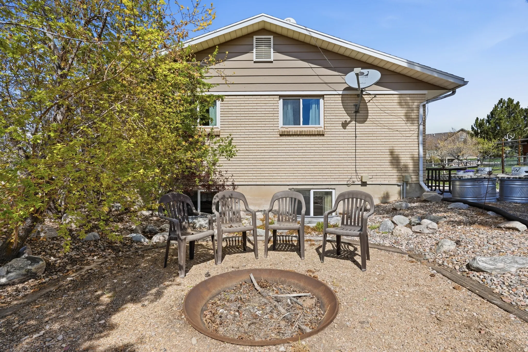 Exterior featuring a fire pit area with gravel ground cover, a natural rock border, and mature landscaping