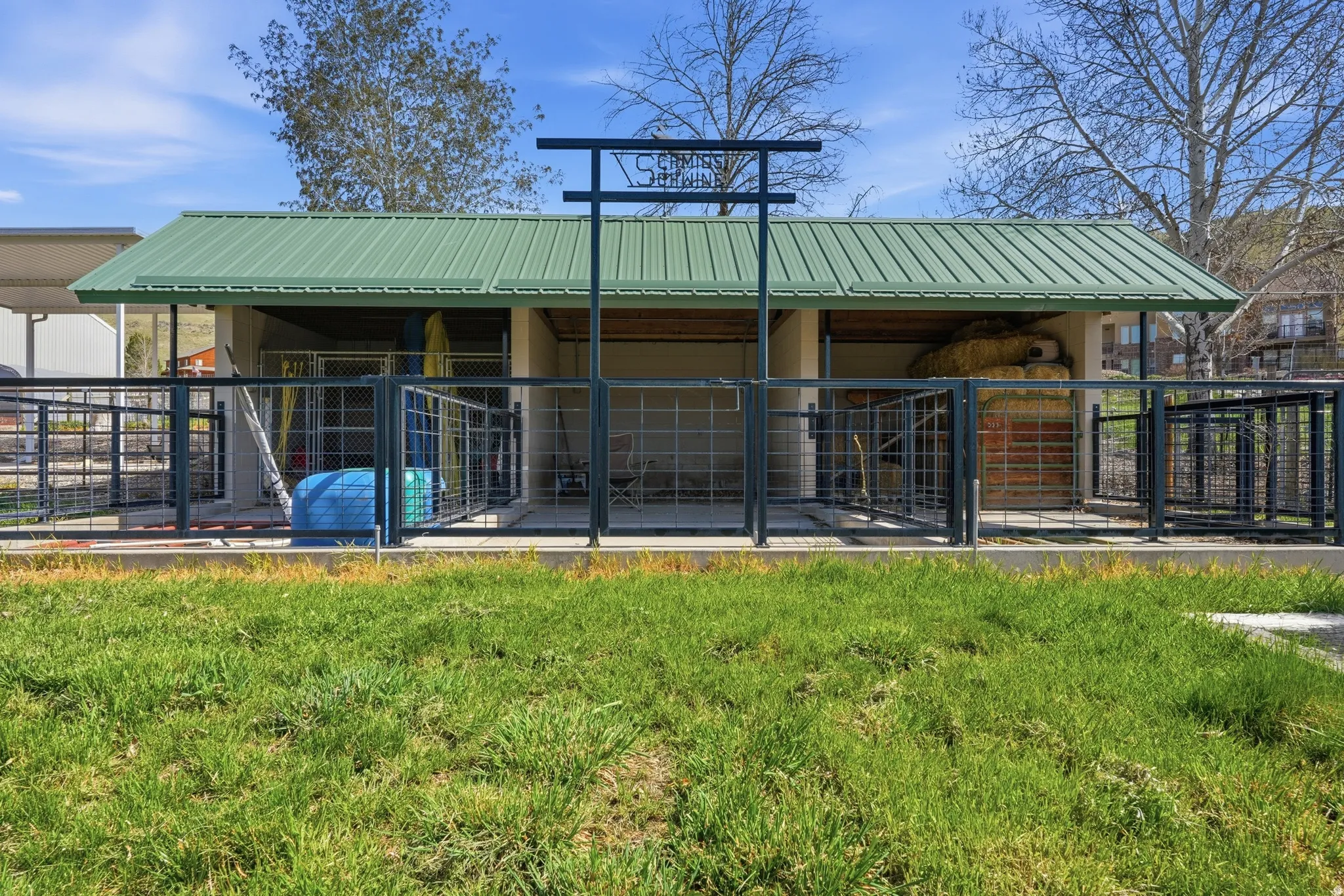 Covered outdoor structure featuring a green metal roof and multiple fenced enclosures