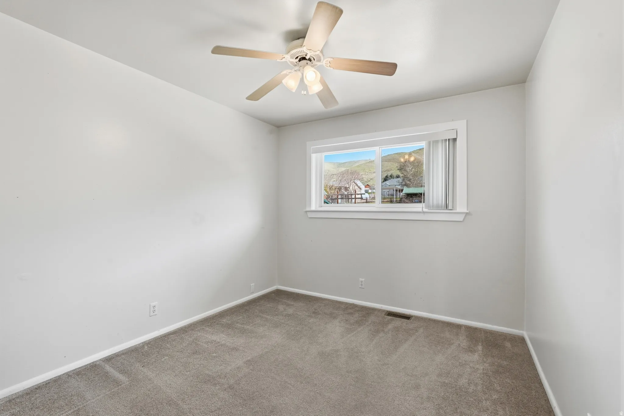Neutral-toned carpeting, ceiling fan with integrated lighting, and a window with white trim