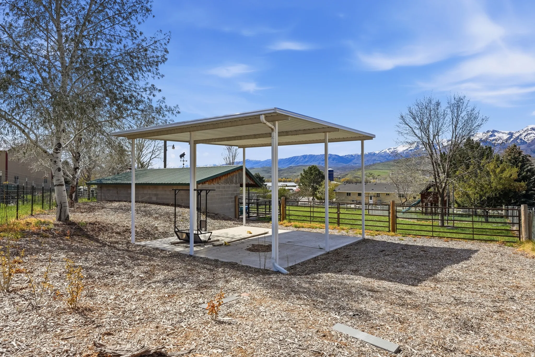 Covered concrete pad, adjacent to a metal fence, with surrounding wood chip ground cover