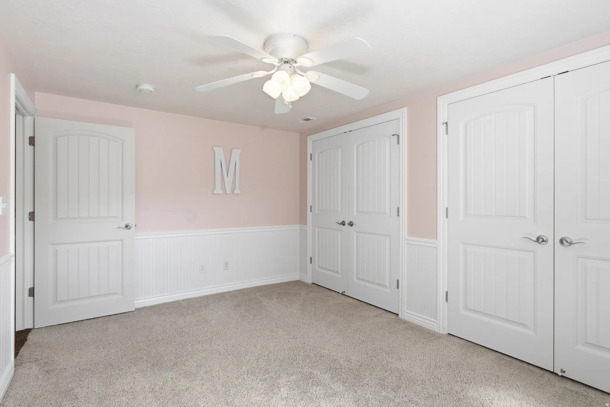 Plush carpeting, beadboard wainscoting, and a ceiling fan with integrated lighting