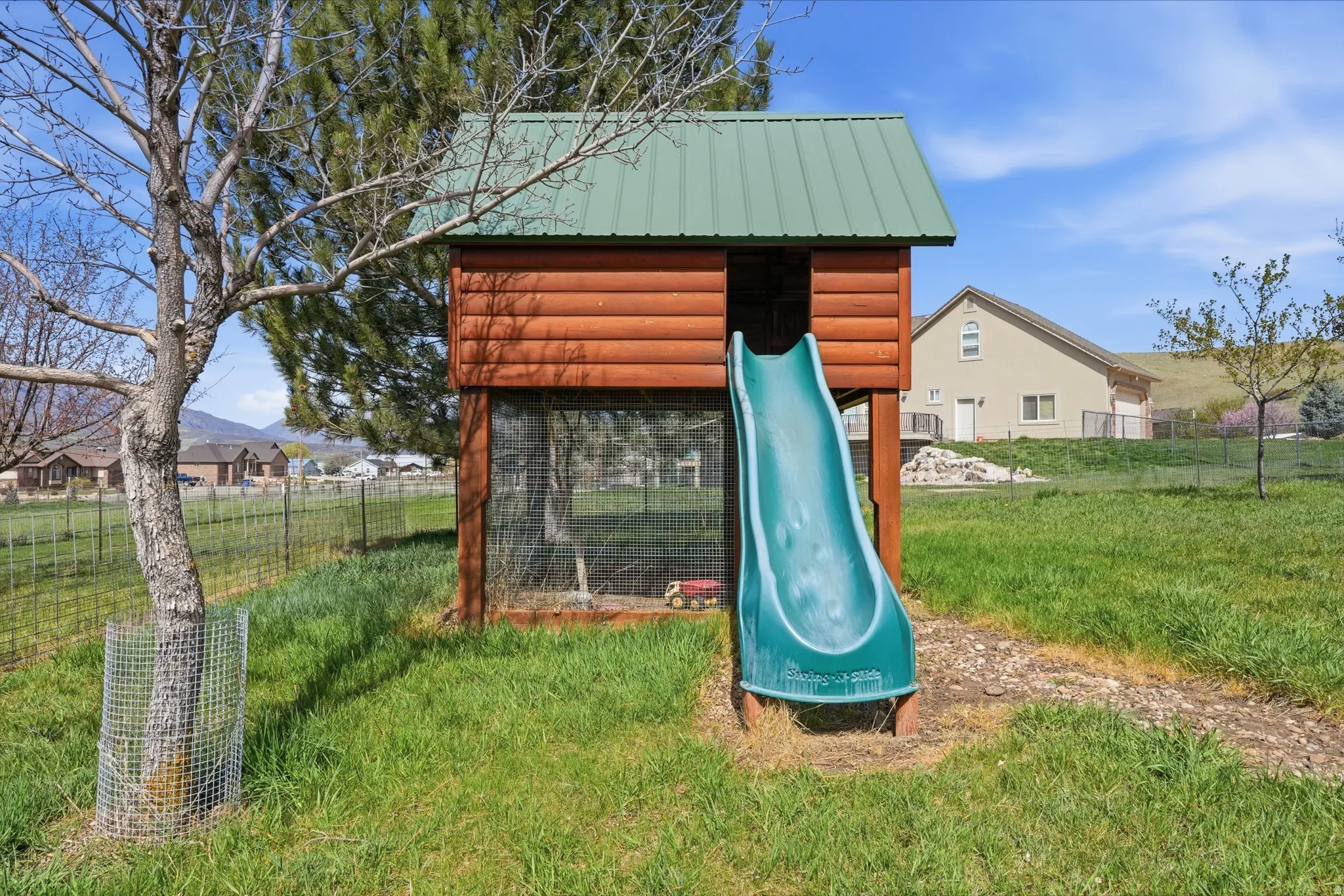 Outdoor play structure featuring a green metal roof, log-style siding, and an attached slide