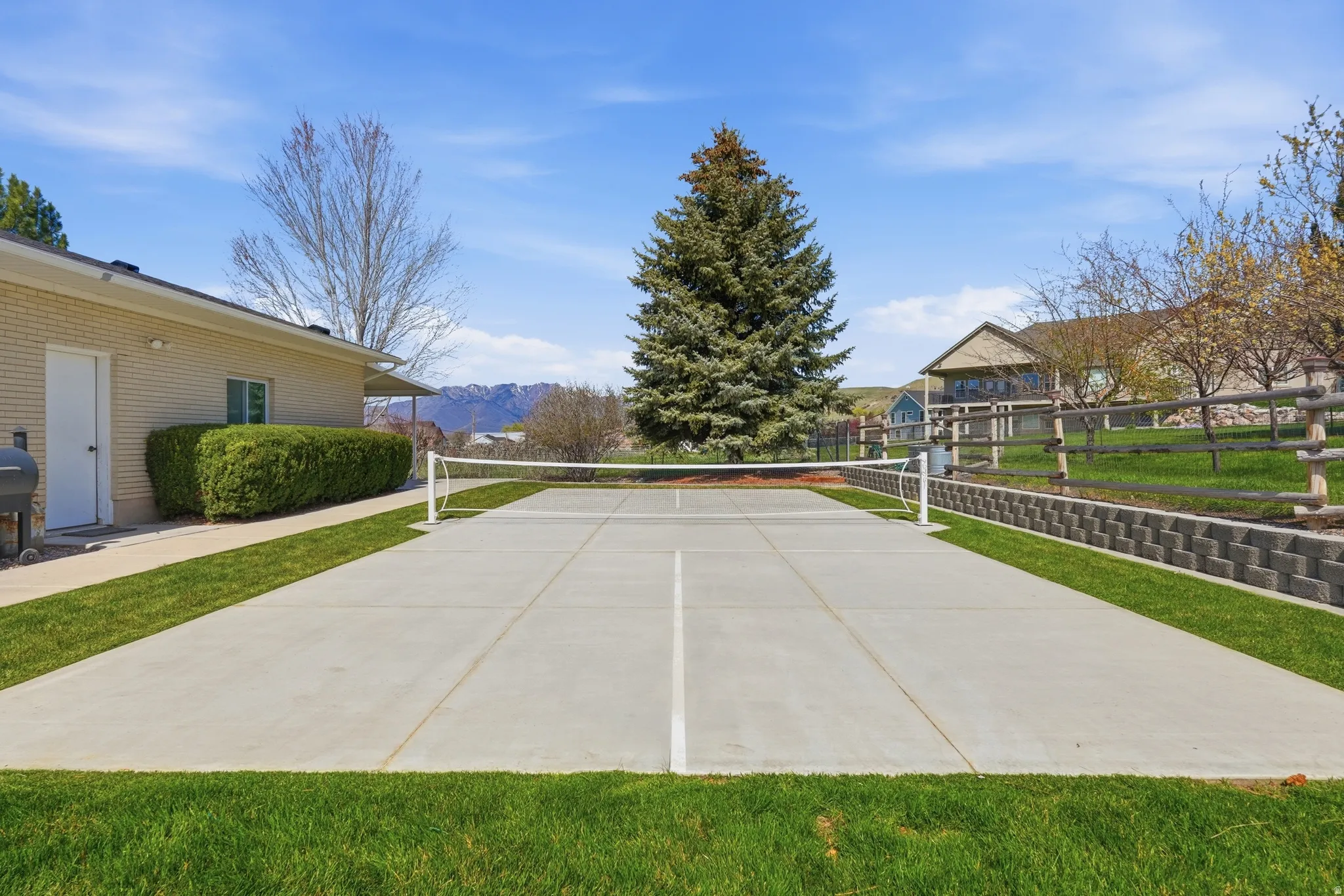 Outdoor sport court with a net, bordered by manicured lawn and a retaining wall