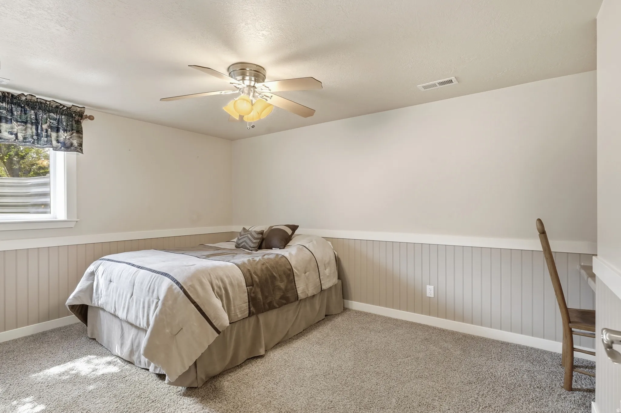 Textured carpet flooring, beadboard wainscoting, and a ceiling fan with integrated lighting