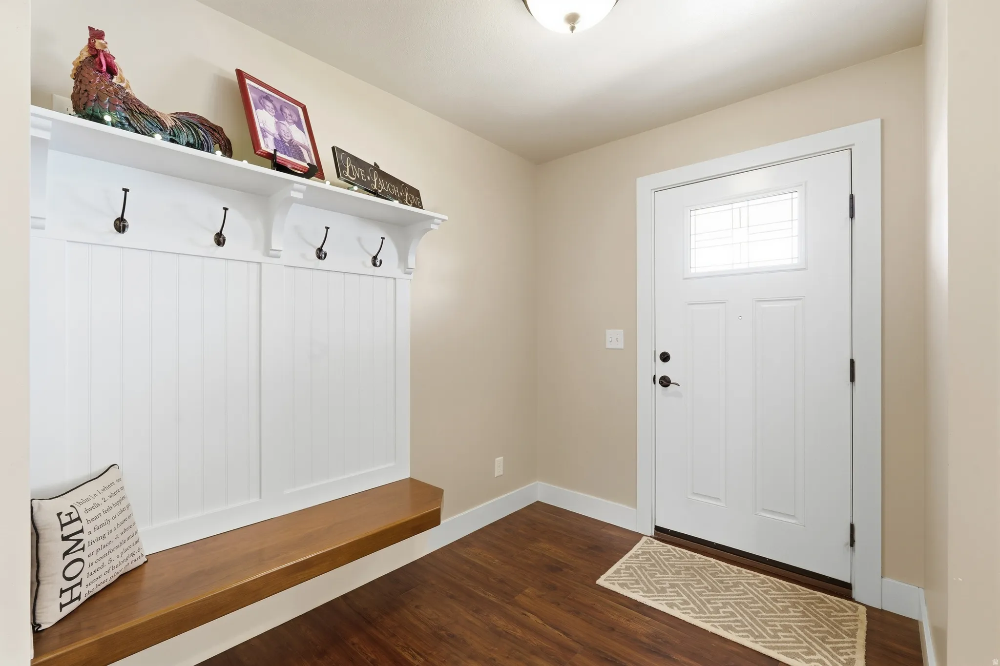 Built-in storage bench with wood surface, white paneling, and four coat hooks